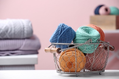 Photo of Colorful clews of threads in basket on table against blurred background, space for text