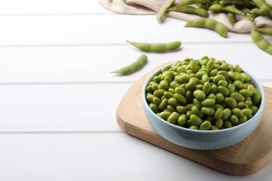 Photo of Bowl of delicious edamame beans on white wooden table, space for text