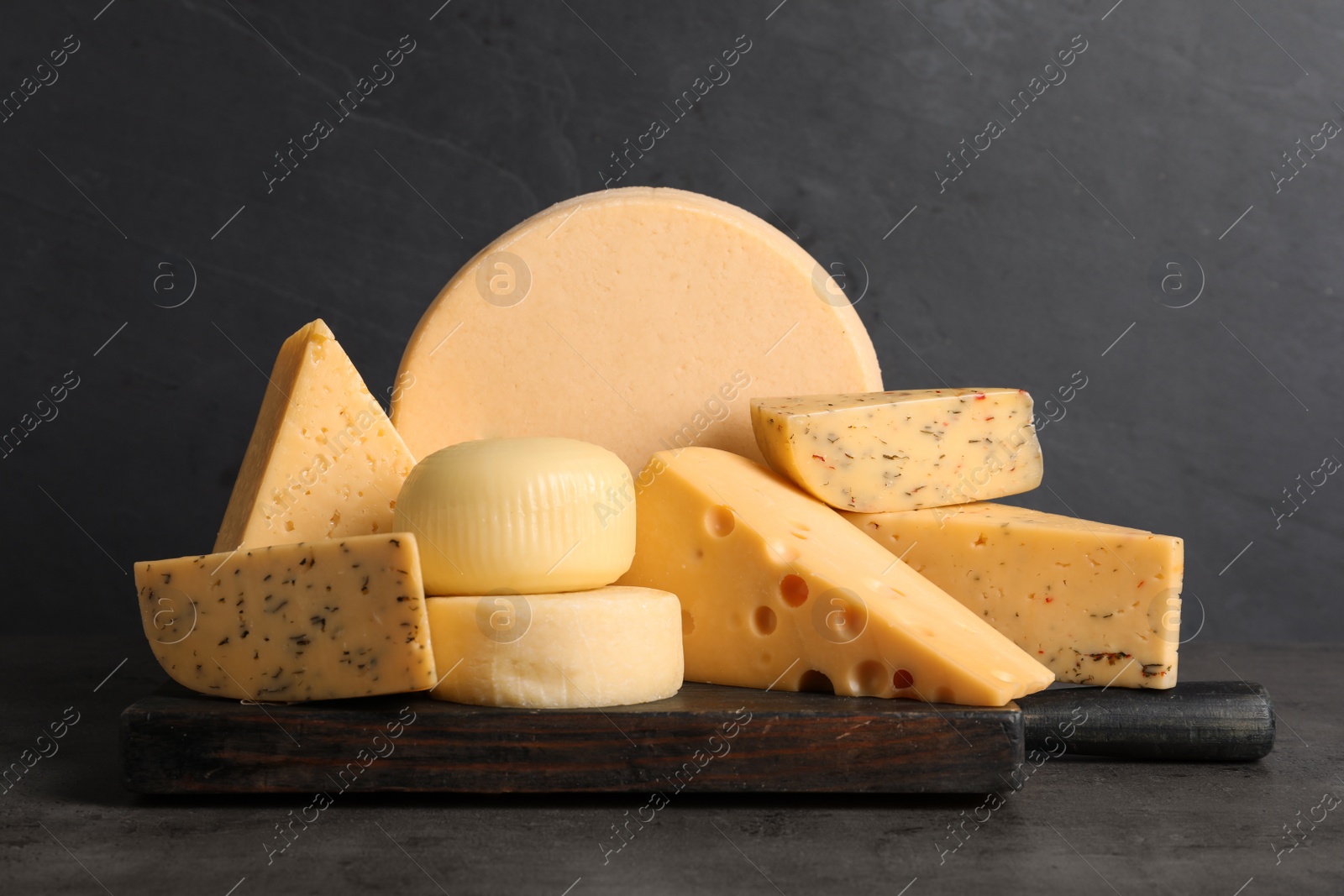 Photo of Wooden board with different sorts of cheese on grey table