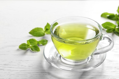 Photo of Cup with hot aromatic mint tea and fresh leaves on table