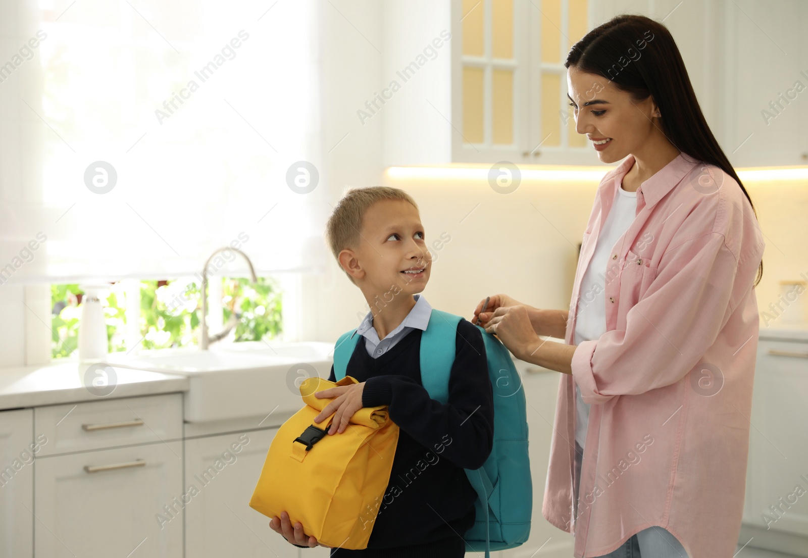 Photo of Young mother helping her little child get ready for school in kitchen