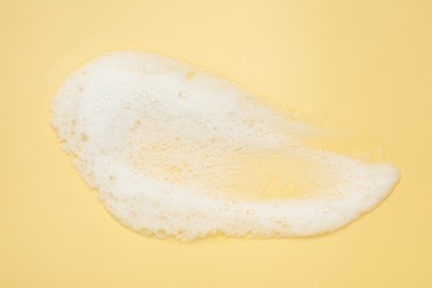 Smudge of white washing foam on yellow background, top view