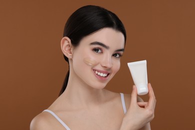 Photo of Teenage girl holding tube with foundation on brown background