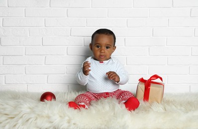 Image of Cute little African American baby with Christmas gift and ball on floor