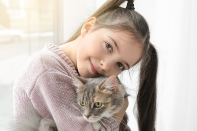 Photo of Cute little girl with cat near window at home