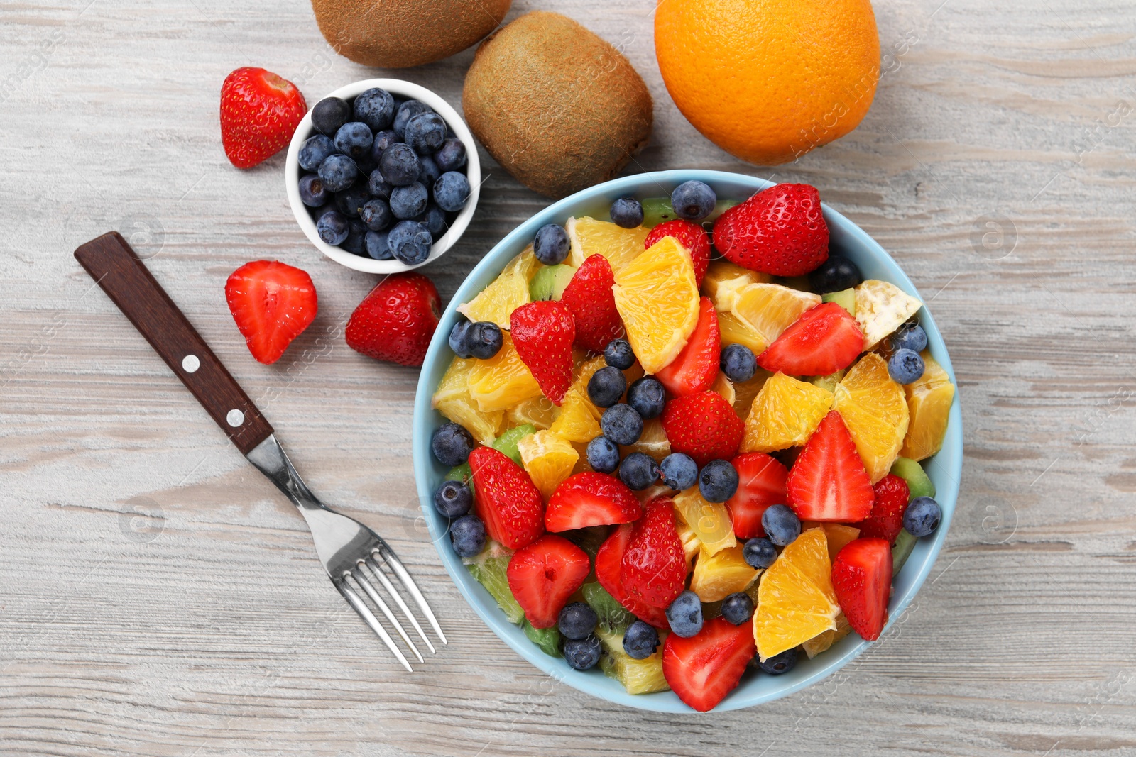 Photo of Delicious fresh fruit salad in bowl served on wooden table, flat lay