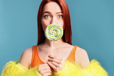 Photo of Redhead woman covering mouth with green lollipop on light blue background