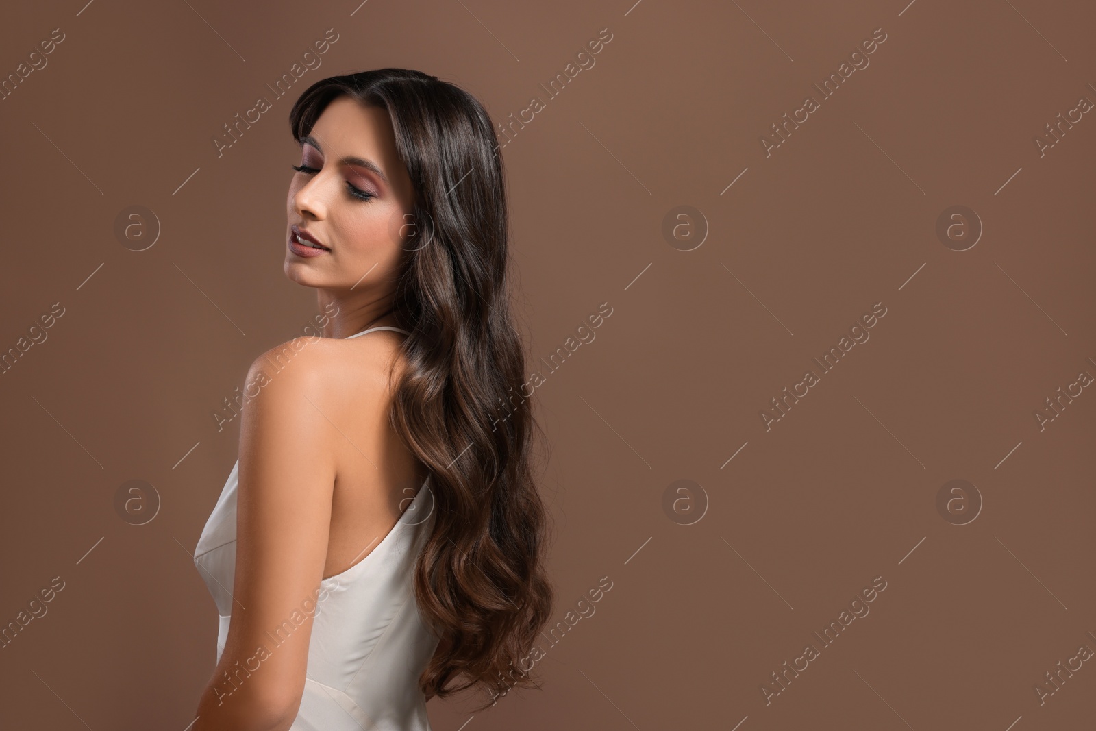 Photo of Hair styling. Beautiful woman with wavy long hair on brown background, space for text
