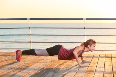 Young woman doing fitness exercises on pier in morning