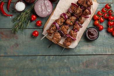 Metal skewers with delicious meat and vegetables served on blue wooden table, flat lay. Space for text