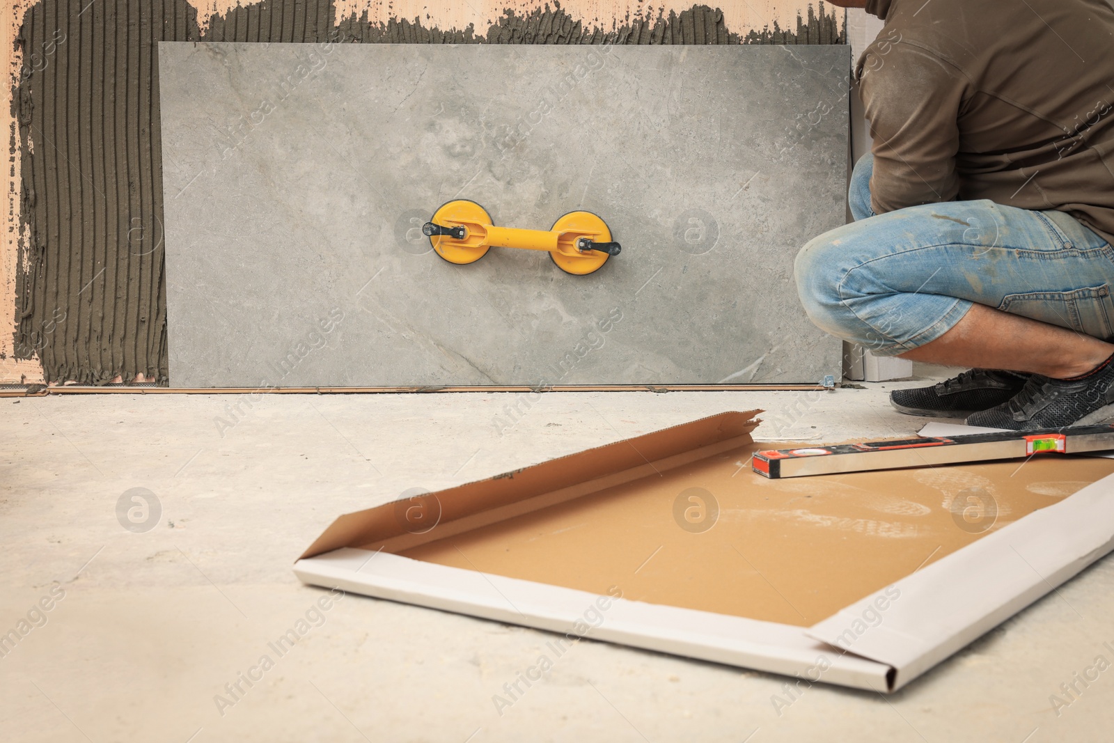 Photo of Professional worker installing tile on wall indoors, closeup