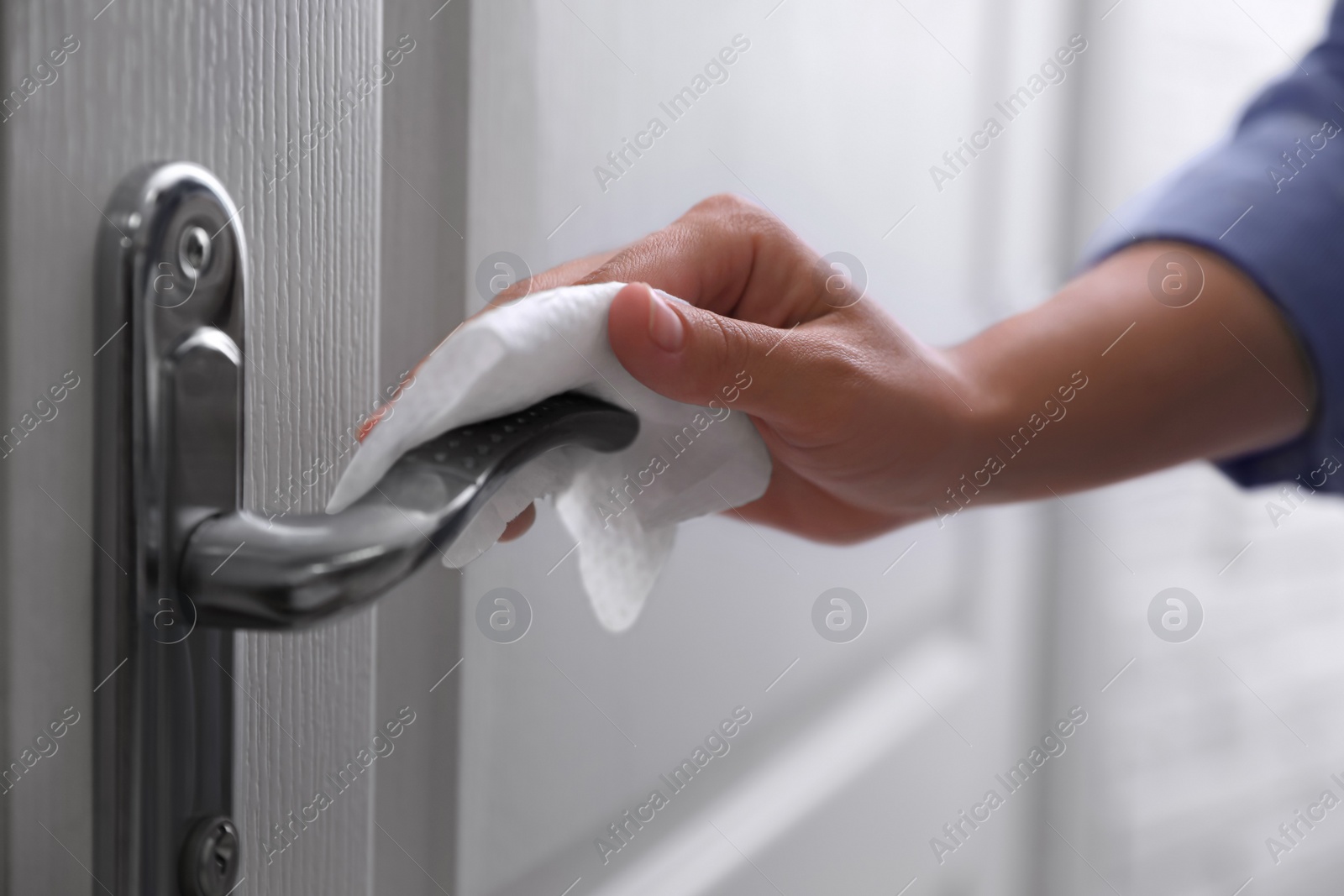 Photo of Woman cleaning door handle with wet wipe indoors, closeup