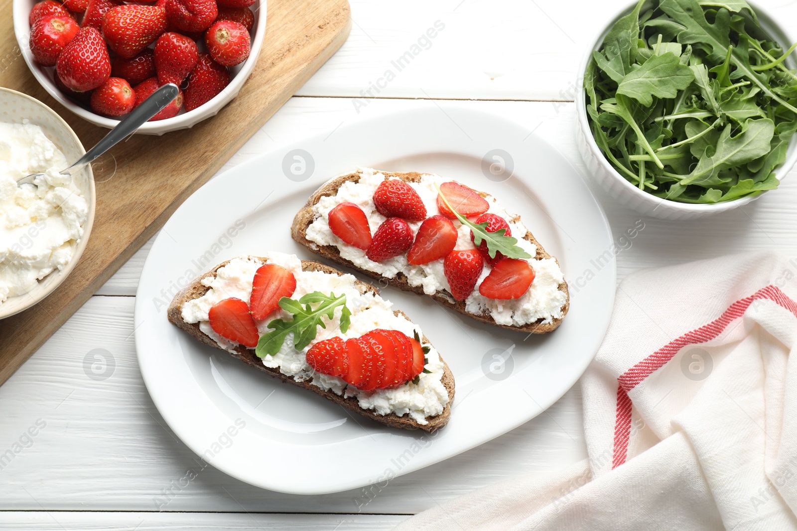 Photo of Delicious ricotta bruschettas with strawberry and arugula on white wooden table, flat lay