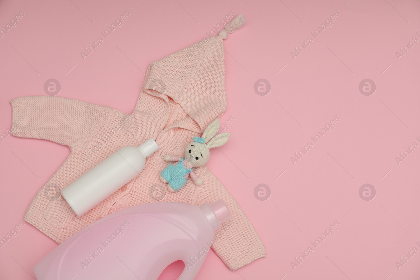 Photo of Bottles of laundry detergents, baby sweatshirt and toy bunny on pink background, flat lay. Space for text