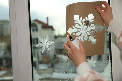 Woman using snow spray for decorating window with snowflakes at home, closeup