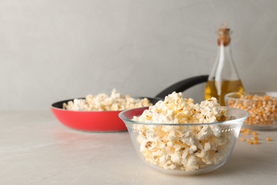 Photo of Glass bowl with tasty popcorn on grey table. Space for text