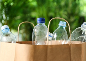 Photo of Paper bag with used plastic bottles against blurred background, closeup. Recycle concept