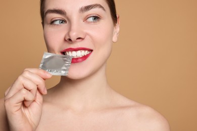 Photo of Woman holding condom on beige background. Safe sex