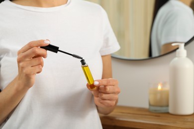 Young woman with eyelash oil near mirror indoors, closeup