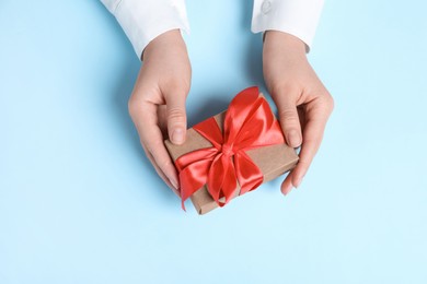 Photo of Woman holding gift box with red bow on light blue background, top view