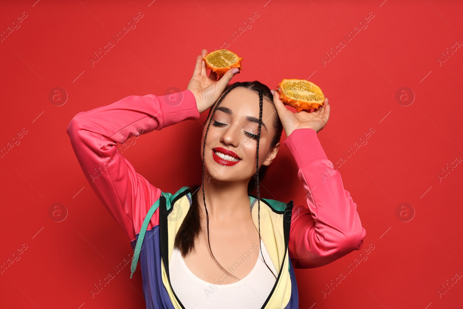 Photo of Young woman with fresh kiwano on red background. Exotic fruit