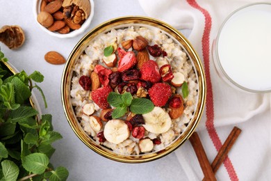 Photo of Delicious oatmeal with freeze dried berries, banana, nuts, mint and milk on white table, flat lay