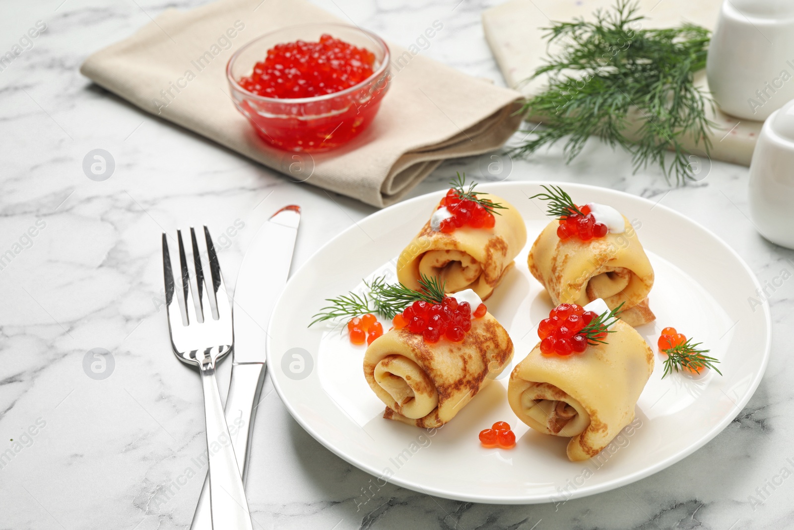 Photo of Delicious thin pancakes with red caviar on white marble table