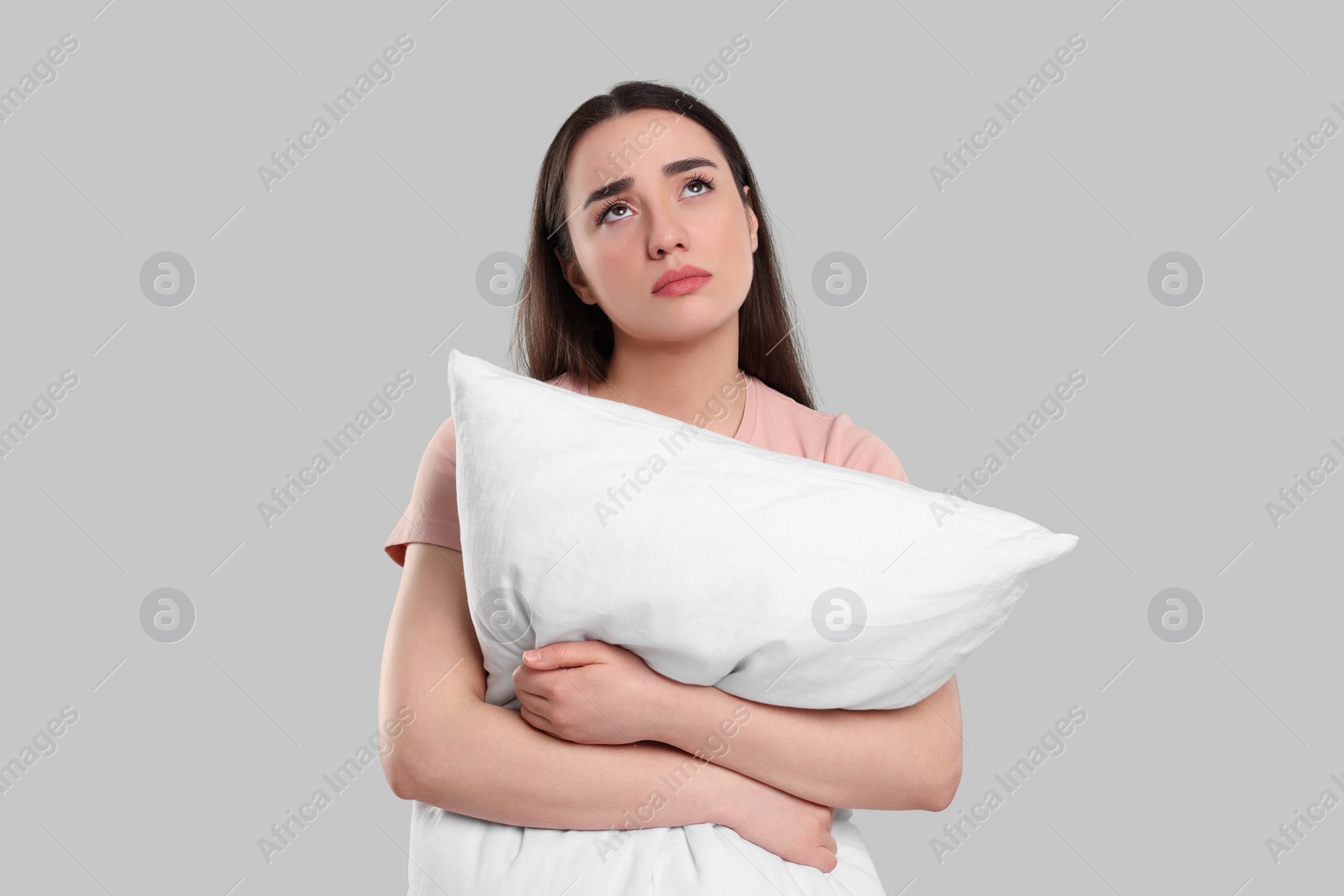 Photo of Tired young woman with pillow on light grey background. Insomnia problem