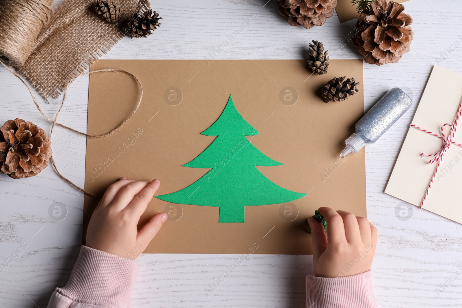 Photo of Little child making Christmas card at white wooden table, top view