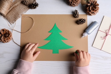 Little child making Christmas card at white wooden table, top view