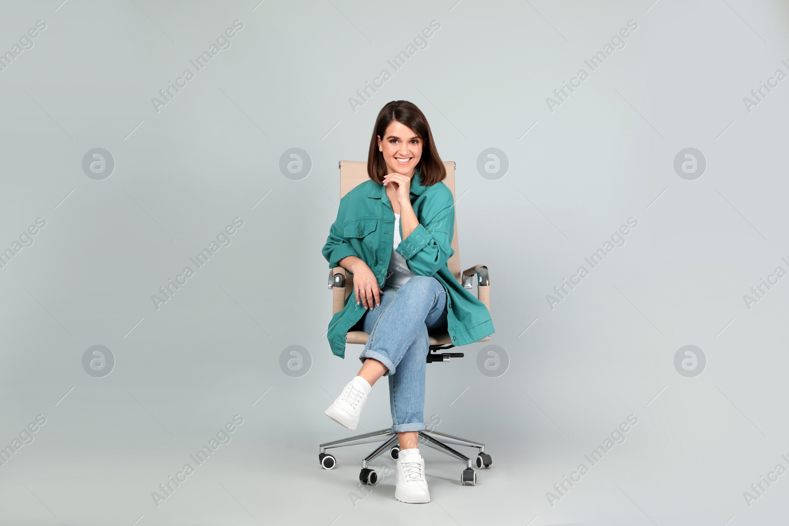 Photo of Young woman sitting in comfortable office chair on grey background