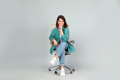 Photo of Young woman sitting in comfortable office chair on grey background