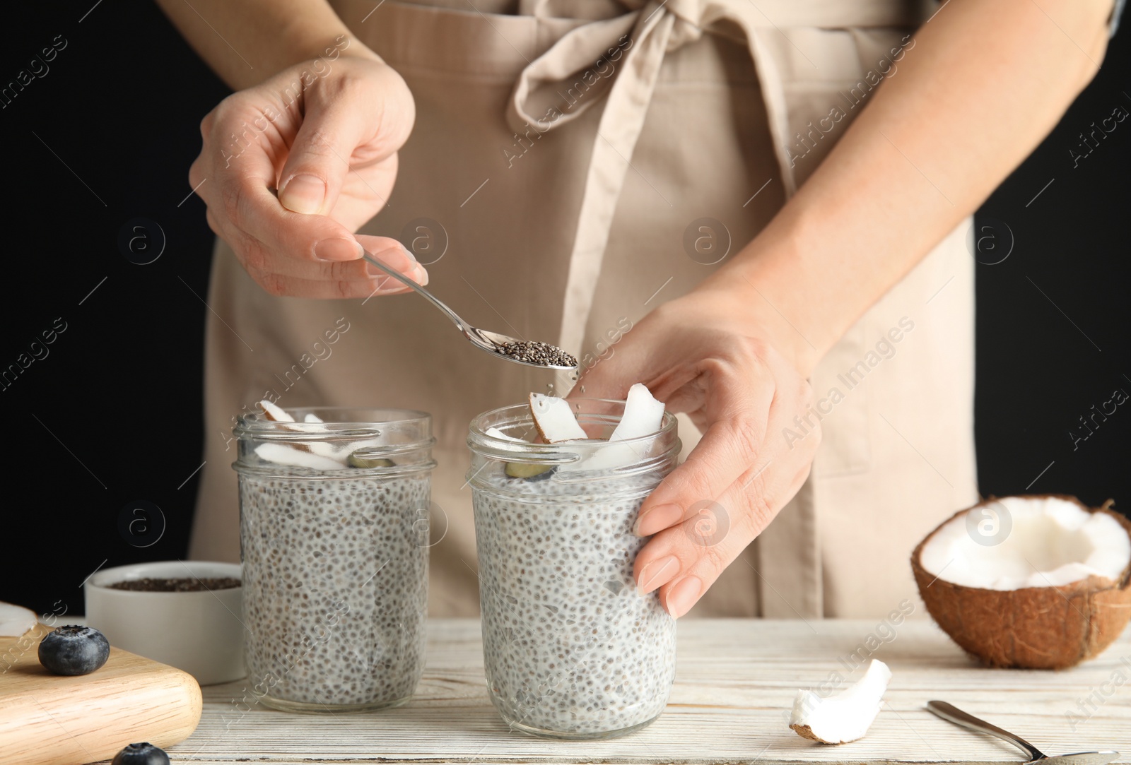 Photo of Young woman preparing chia seed pudding with coconut at table