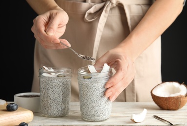 Photo of Young woman preparing chia seed pudding with coconut at table