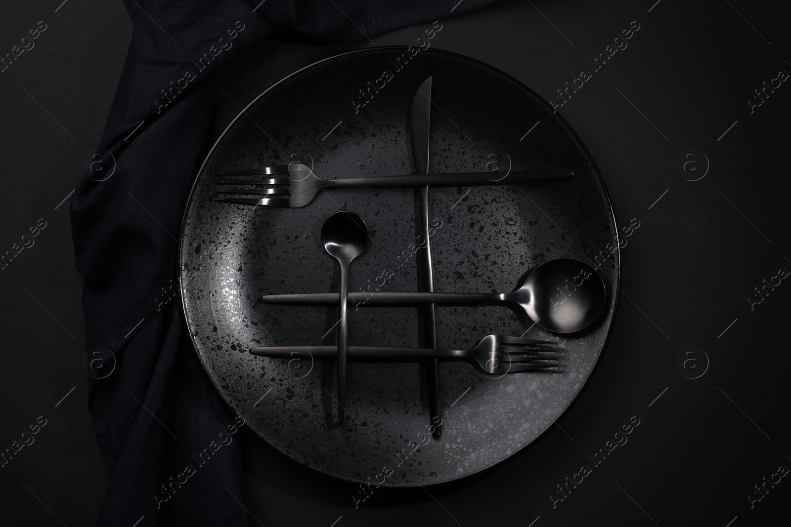 Photo of Stylish table setting. Plate, napkin and cutlery on black background, top view