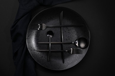 Stylish table setting. Plate, napkin and cutlery on black background, top view