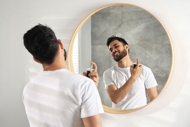 Photo of Man spraying luxury perfume near mirror indoors