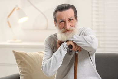 Senior man with walking cane on sofa at home