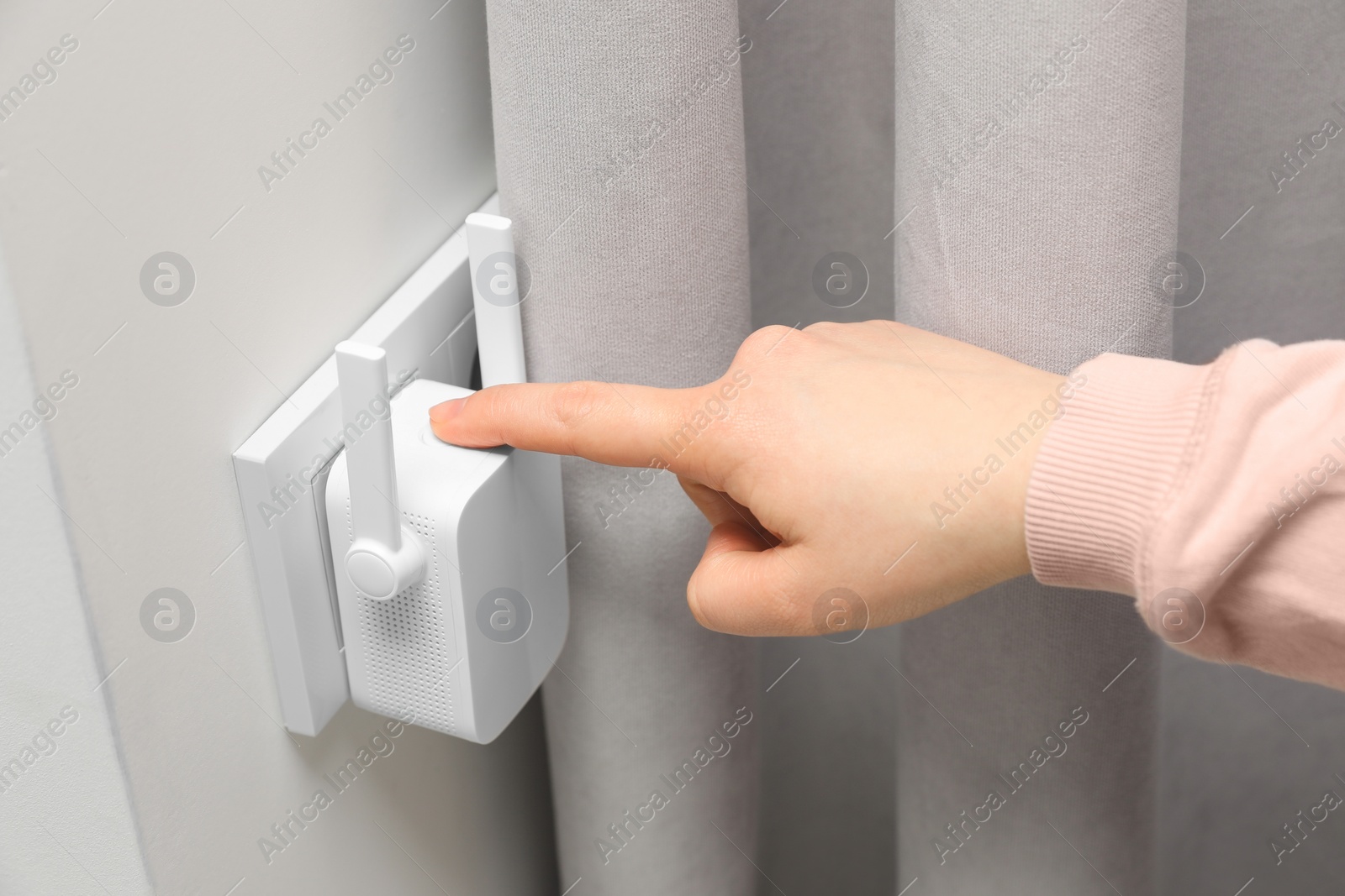 Photo of Woman turning on wireless Wi-Fi repeater indoors, closeup