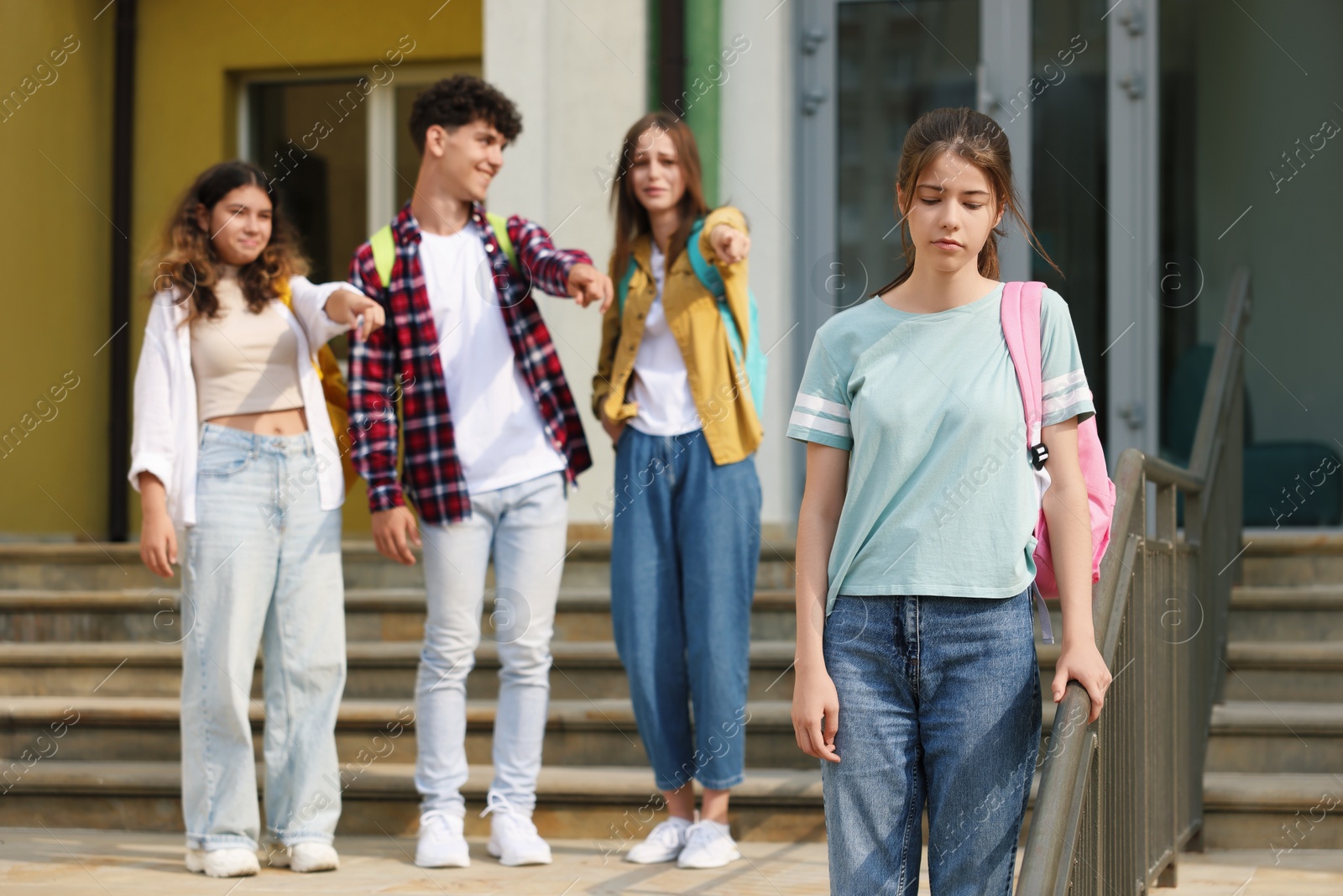 Photo of Teen problems. Group of students pointing at upset girl outdoors, selective focus