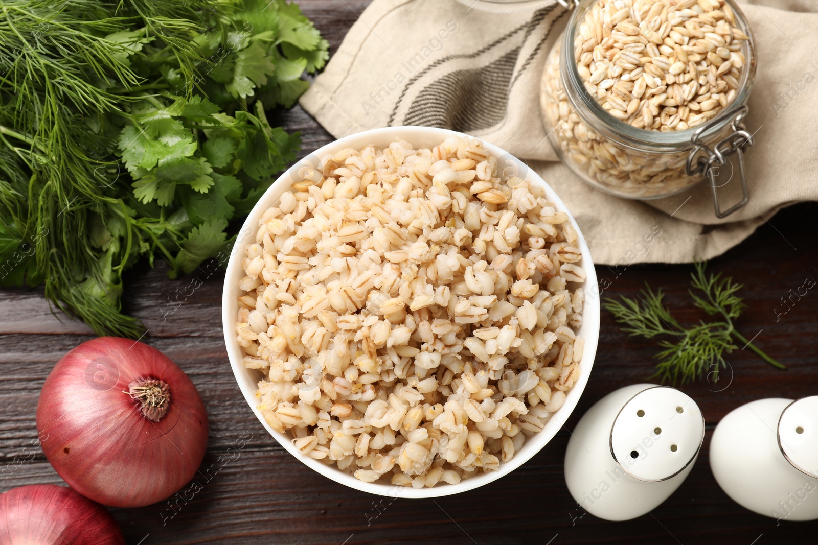 Photo of Delicious pearl barley in bowl served on wooden table, flat lay