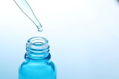 Dripping liquid from pipette into glass bottle on light blue background, closeup. Space for text