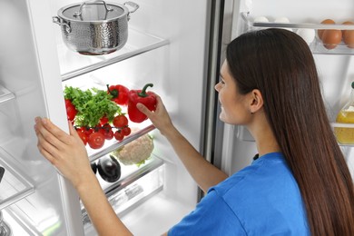 Young woman taking red bell pepper out of refrigerator