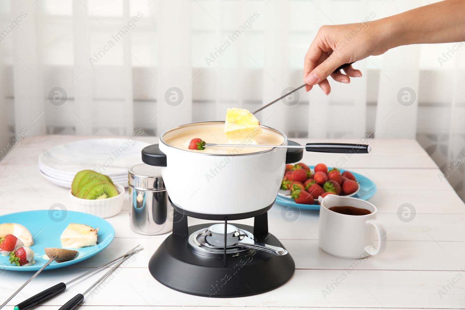 Photo of Woman dipping pineapple into pot with white chocolate fondue on table