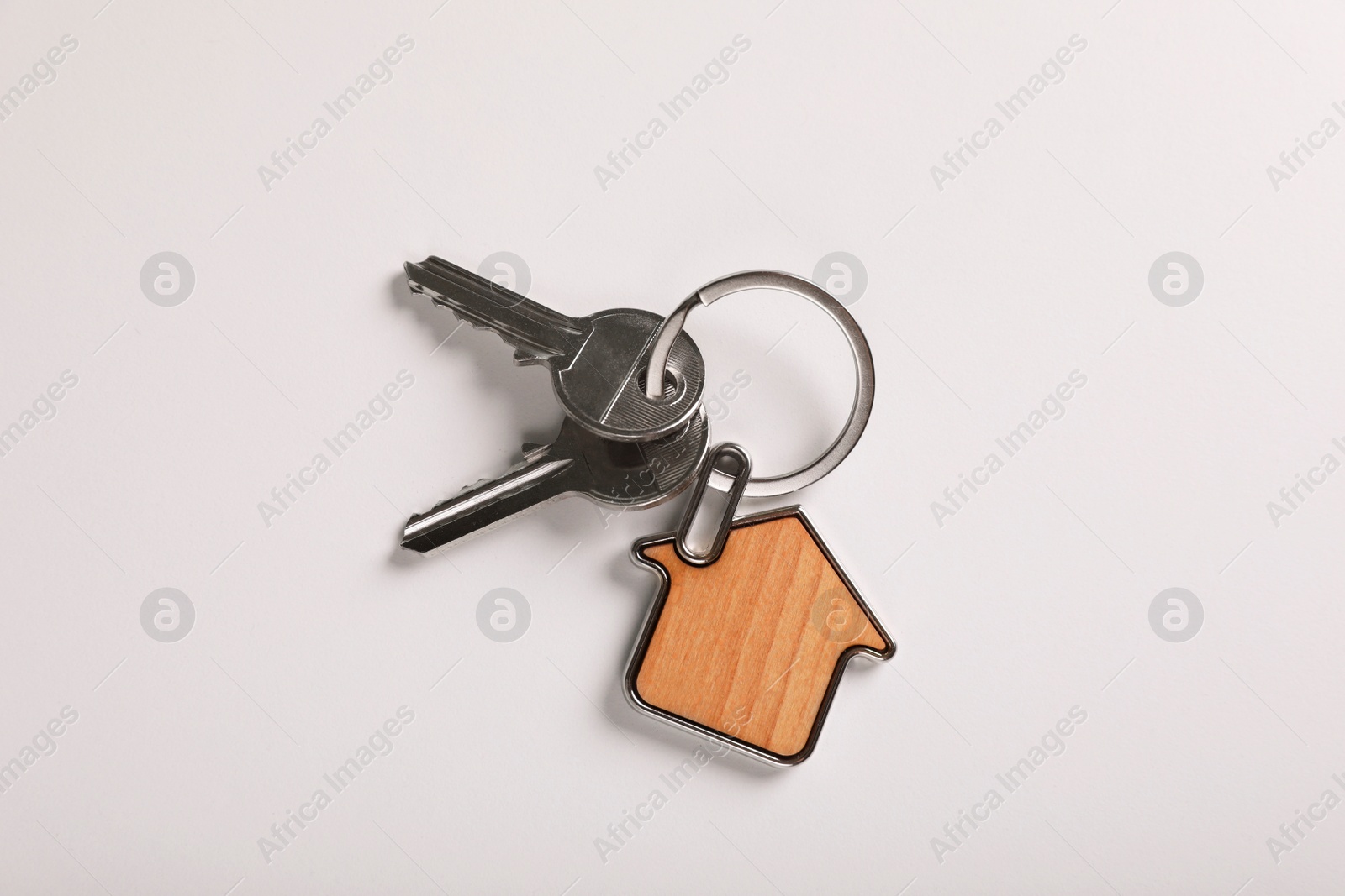 Photo of Keys with trinket in shape of house on white background, top view. Real estate agent services