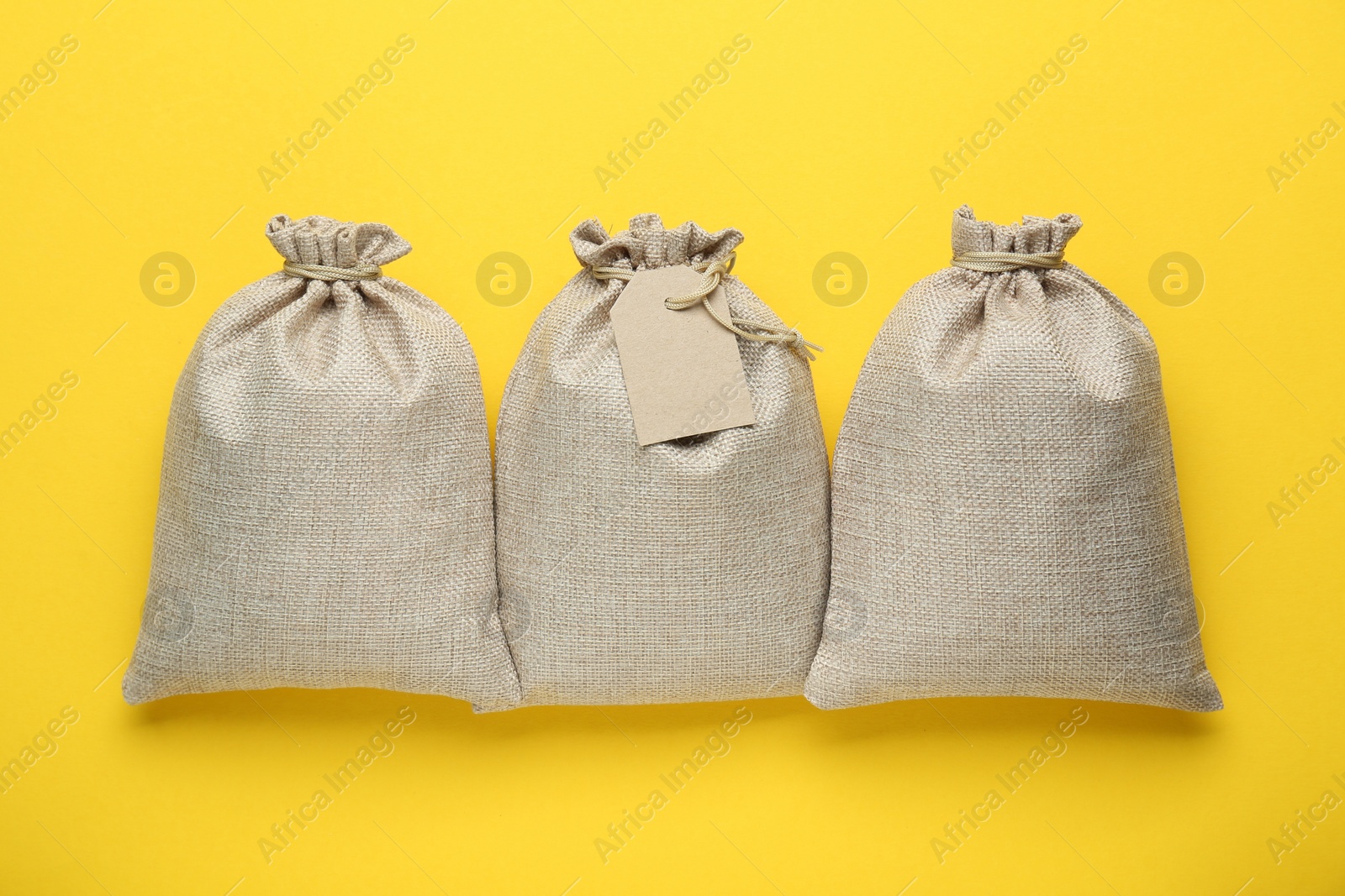 Photo of Tied burlap bags on yellow background, top view