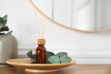 Reed diffuser and home decor on wooden table near white wall