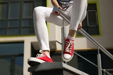 Photo of Woman in red classic old school sneakers sitting on railing outdoors, closeup