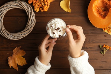 Photo of Woman holding straw and glass with pumpkin spice latte on wooden background, top view