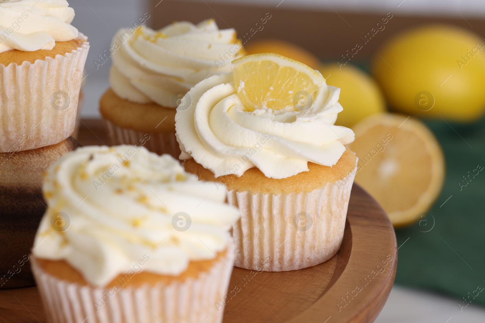 Photo of Delicious lemon cupcakes with white cream on wooden stand, closeup